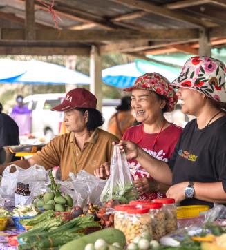Market vendors smiling behind a table of fresh produce.