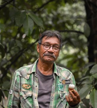 Man in a plaid shirt holding a white object, standing in a Moreganic forest.